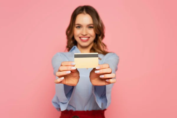 Tarjeta de crédito en manos de una mujer sonriente sobre fondo borroso aislado en rosa - foto de stock