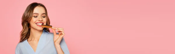 Улыбающаяся женщина кусает кредитную карту изолированы на розовый, баннер — стоковое фото