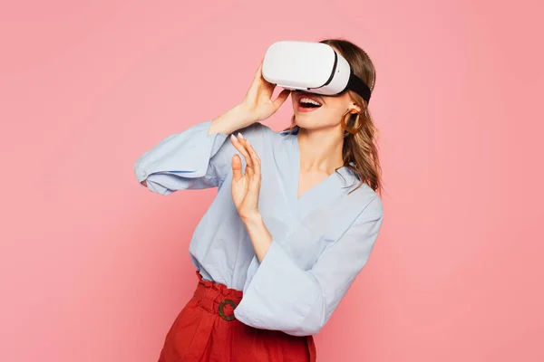 Улыбающаяся женщина с помощью наушников виртуальной реальности, изолированных на розовый — стоковое фото