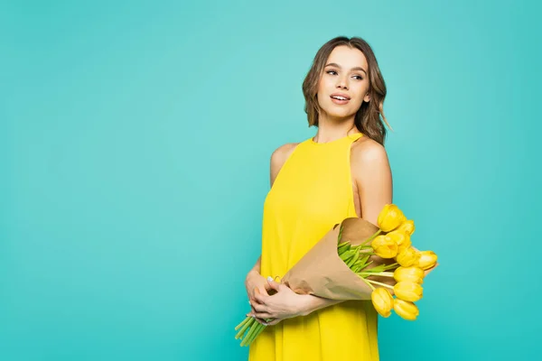 Pretty woman holding bouquet of yellow tulips isolated on blue — Stock Photo