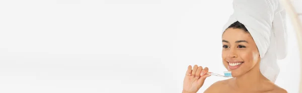 Smiling young african american woman wrapped in towel holding toothbrush near face in bathroom, banner — Stock Photo