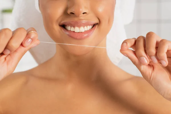 Vista parcial de la joven afroamericana sonriente sosteniendo hilo dental en las manos cerca de la cara sobre fondo blanco - foto de stock