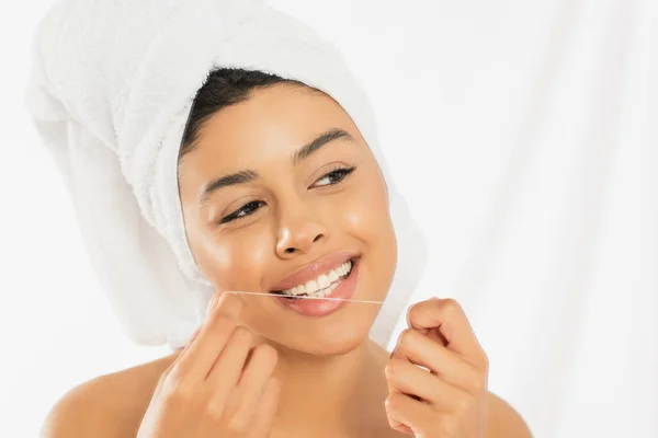 Joven afroamericana mujer envuelta en toalla limpieza de dientes con hilo dental sobre fondo blanco — Stock Photo
