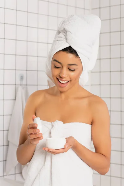 Heureux jeune femme afro-américaine ouverture pot de crème dans la salle de bain — Photo de stock