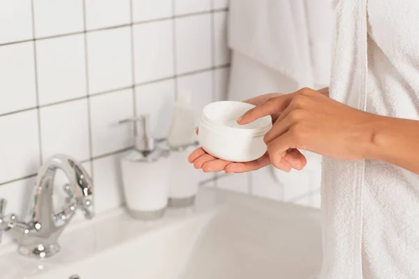 Vista da vicino della giovane donna afroamericana che tocca la crema in vaso con il dito in bagno — Foto stock