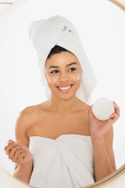 Young african american woman wrapped in towels holding cream jar in bathroom — Stock Photo