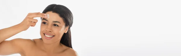 Jeune femme afro-américaine souriante appliquant de la crème sur le front sur fond blanc, bannière — Photo de stock