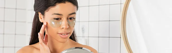 Joven afroamericana mujer de la mano cerca de la cara con parches en los ojos en el baño, pancarta - foto de stock