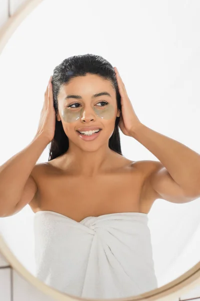 Mujer afroamericana joven con parches en los ojos tomados de la mano en la cabeza en el baño - foto de stock