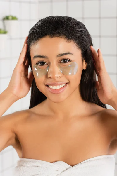 Smiling young african american woman with eye patches holding hands on head in bathroom — Stock Photo