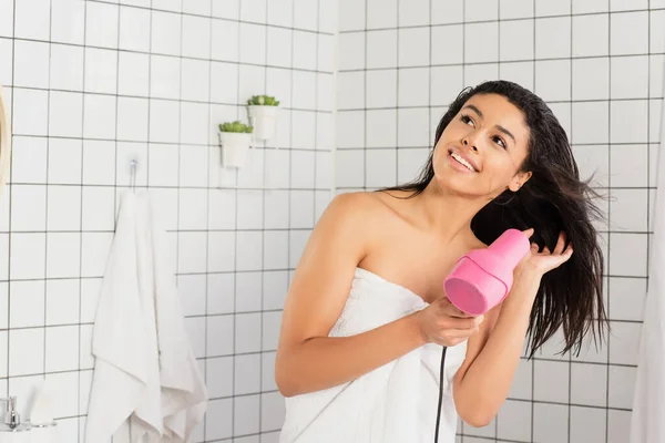 Young african american woman wrapped in towel styling hair with dryer in bathroom — Stock Photo