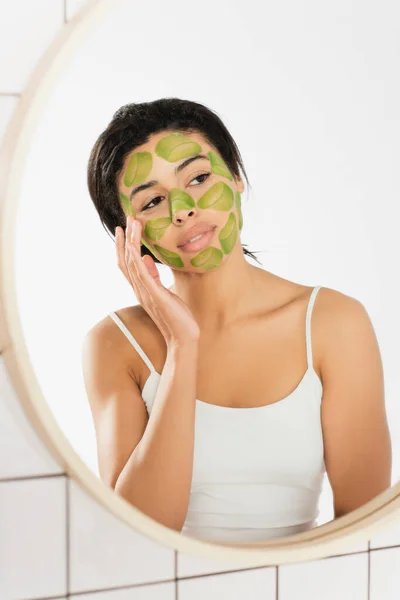 Junge Frau berührt Gesicht mit grüner Maske nahe Fenster im Badezimmer — Stockfoto