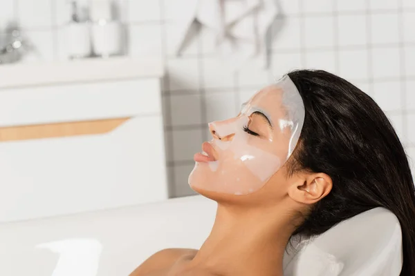 Young african american woman with sheet mask on face lying in bathtub — Stock Photo