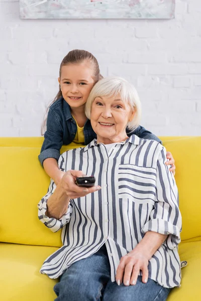 Lächelndes Kind umarmt Großmutter vor dem Fernseher zu Hause — Stockfoto