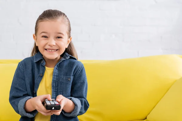 Happy girl holding remote controller and looking at camera — Stock Photo