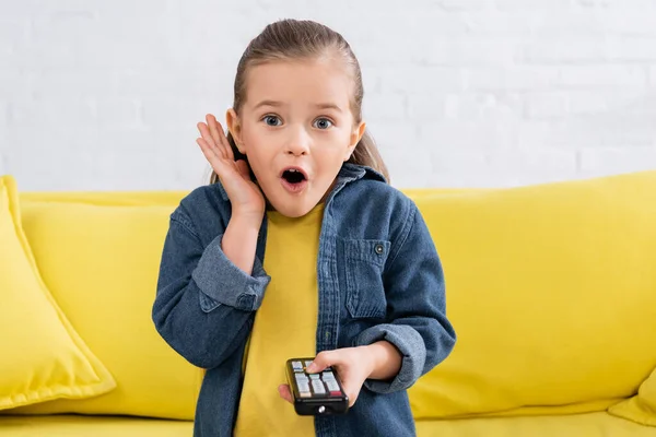 Verblüfftes Kind mit Fernbedienung auf Couch — Stockfoto