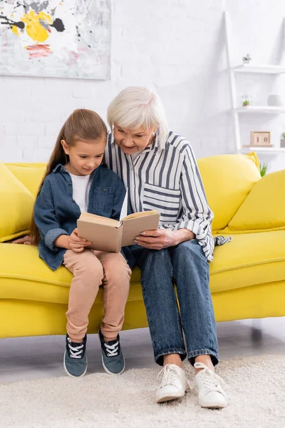 Sorridente nonna e bambino lettura libro insieme sul divano — Foto stock