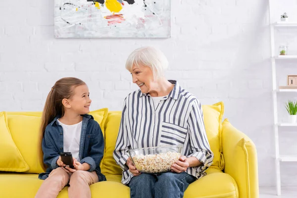 Enfant souriant avec télécommande regardant mamie avec pop-corn — Photo de stock