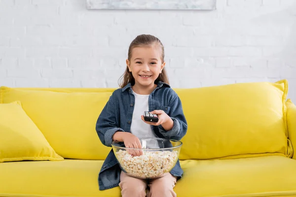 Smiling girl with remote controller taking popcorn from bowl — Stock Photo