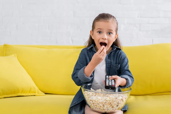 Aufgeregtes Mädchen mit Fernbedienung isst Popcorn — Stockfoto