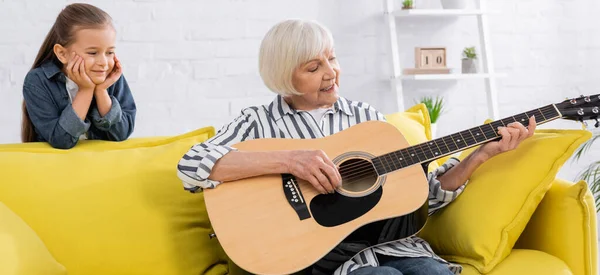 Positive Seniorin spielt Akustikgitarre neben Enkelin, Banner — Stockfoto