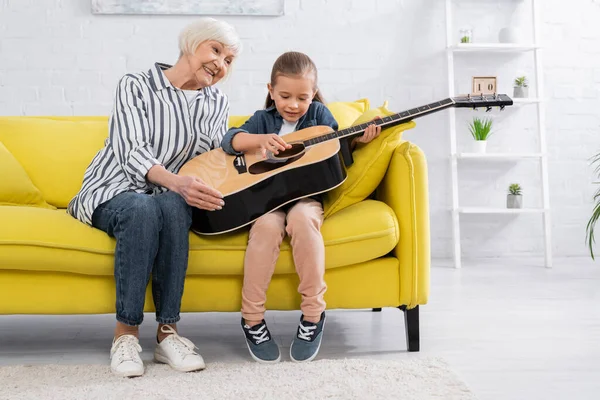 Lächelndes Kind spielt Akustikgitarre neben Großeltern auf Sofa — Stockfoto