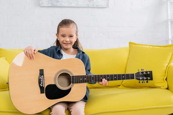 Niño con guitarra acústica sonriendo a la cámara en casa - foto de stock