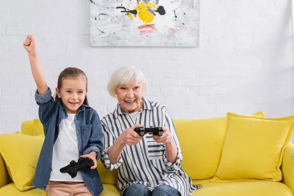 KYIV, UCRANIA - 11 de enero de 2021: Muchacho sonriente mostrando sí gesto cerca de la abuela con joystick - foto de stock