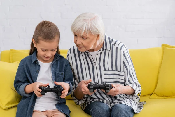 QUIIV, UCRÂNIA - JANEIRO 11, 2021: Criança usando gamepad perto da avó no sofá — Fotografia de Stock