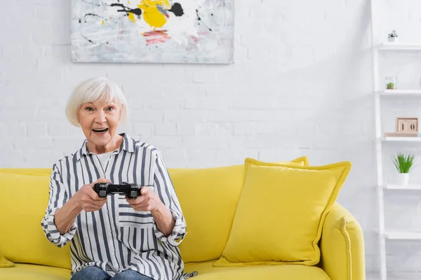 KYIV, UKRAINE - 11 JANVIER 2021 : Femme âgée souriante jouant à un jeu vidéo à la maison — Photo de stock