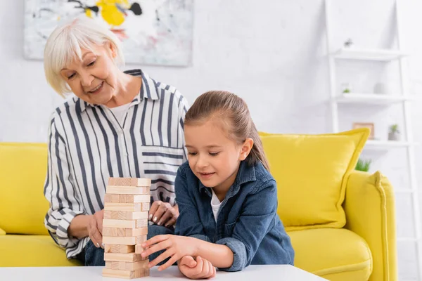 Souriant fille jouer blocs bois jeu près floue mamie — Photo de stock