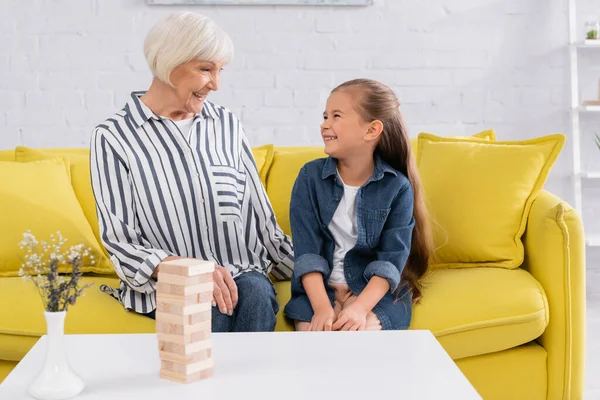 Blocks wood game on coffee table near cheerful granny and kid looking at each other — Stock Photo