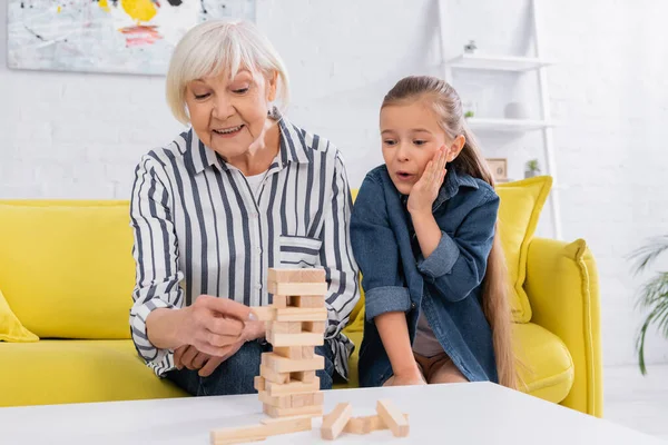 Aufgeregtes Mädchen schaut lächelnde Oma an, die Holzblöcke spielt — Stockfoto