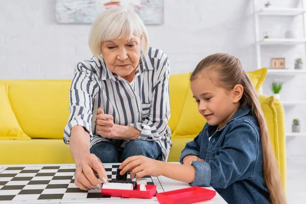 Senior woman taking checkers near board and granddaughter — Stock Photo