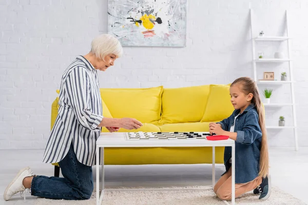 Niño jugando damas con abuelos mayores en la mesa de café - foto de stock