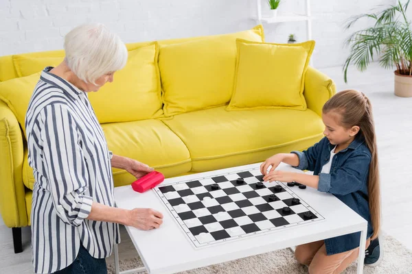 Child and grandparent playing checkers game on board — Stock Photo