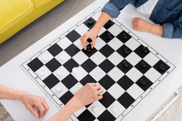 Cropped view of elderly woman and child playing checkers at home — Stock Photo