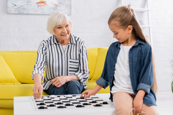 Lächelnde ältere Frau beim Schachspiel mit verschwommener Enkelin — Stockfoto