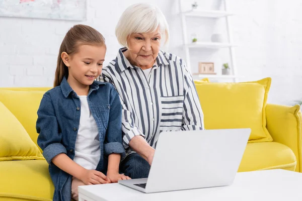Femme âgée et enfant utilisant un ordinateur portable sur la table basse à la maison — Photo de stock