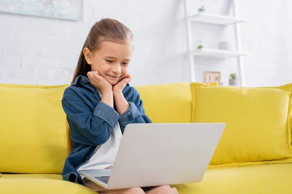 Ragazza sorridente guardando il computer portatile sul divano giallo — Foto stock