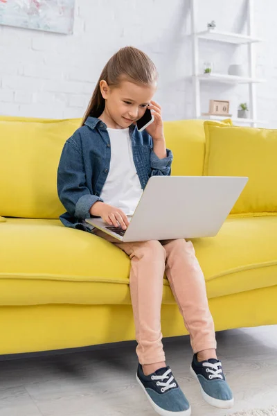 Criança falando no smartphone e usando laptop na sala de estar — Fotografia de Stock