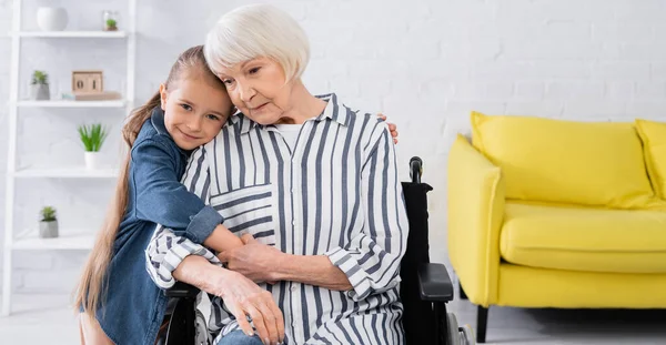 Sonriente niño abrazando a la abuela en silla de ruedas, bandera - foto de stock