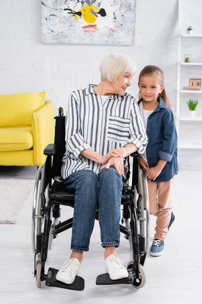 Smiling woman in wheelchair looking at granddaughter at home — Stock Photo