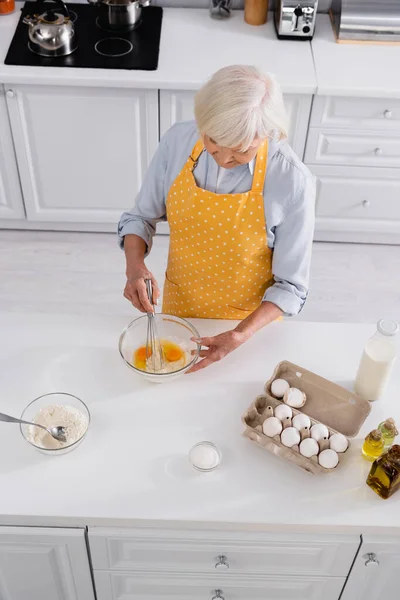 Vista aérea de la mujer anciana mezclando ingredientes en un tazón mientras cocina - foto de stock