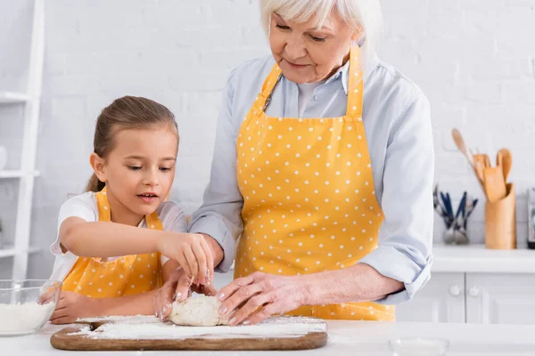 Kind und Oma in Schürzen machen gemeinsam Teig in der Küche — Stockfoto