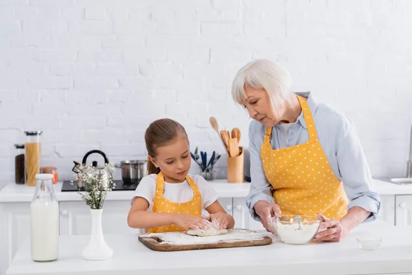 Mamie tenant la farine tandis que l'enfant faisant la pâte près du lait dans la cuisine — Photo de stock