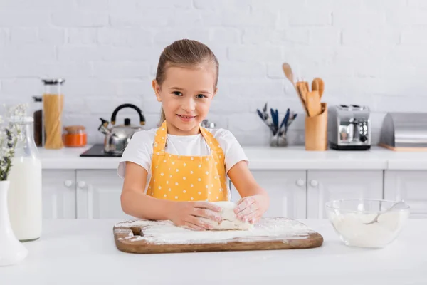 Счастливая девушка в фартуке готовит тесто рядом с ингредиентами — стоковое фото