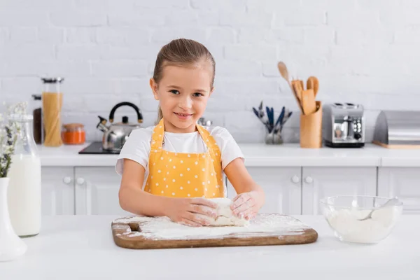 Chica feliz en delantal preparando la masa cerca de los ingredientes - foto de stock