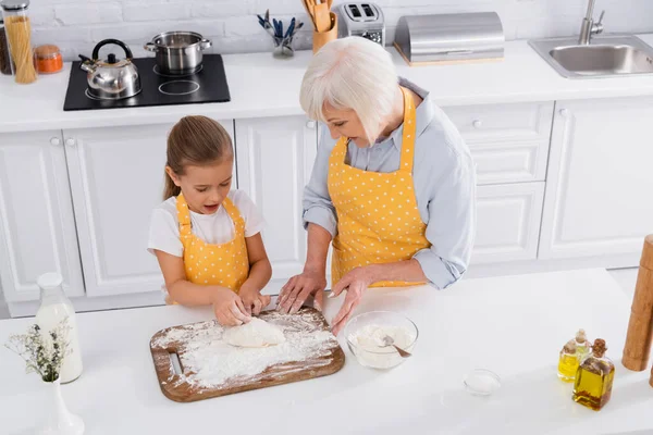 Overhead view of smiling granny helping to child with dough in kitchen — Stock Photo