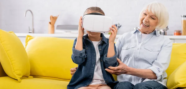 Kind im Kopfhörer sitzt neben Oma auf Couch im Wohnzimmer, Banner — Stockfoto